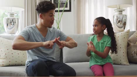 Happy-biracial-father-and-daughter-sitting-on-sofa-using-sign-language