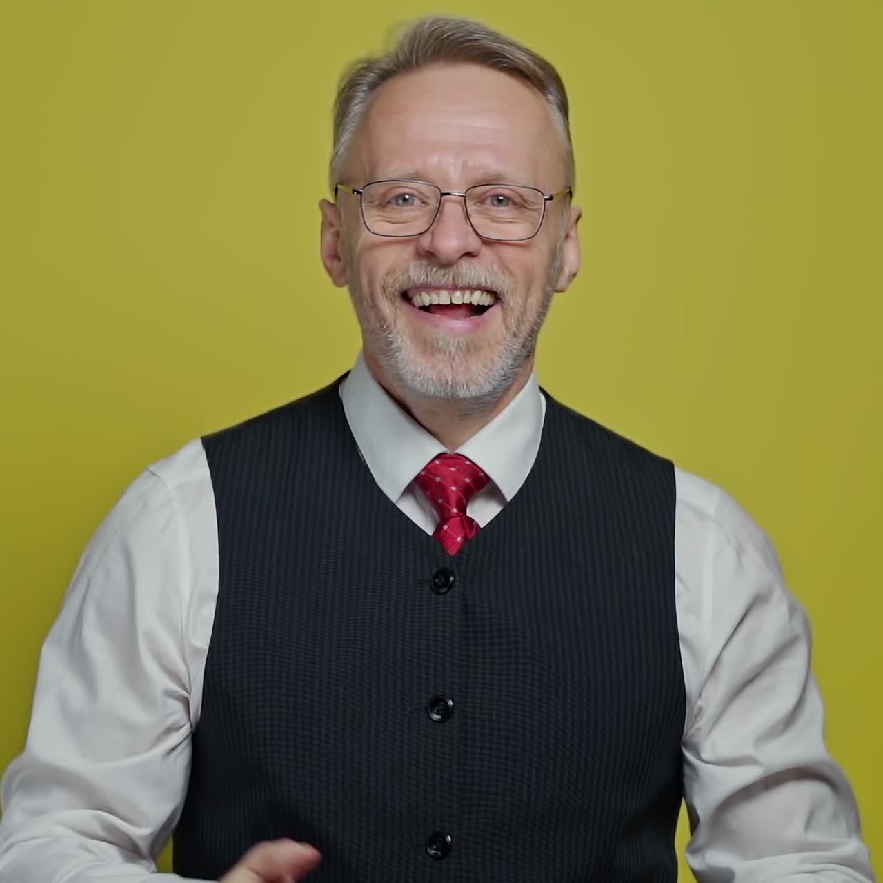 Portrait of smiling mature man in glasses. Happy senior grey-haired man in white shirt and tie looks at camera and talk in studio.