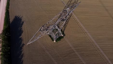 aerial close up of high voltage pylon for electricity transportation in the middle of a plowed field