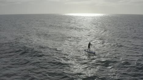 Hombre-En-Stand-Up-Paddleboard-Silueteado-En-Rayo-De-Sol-Y-Oleaje-Del-Océano