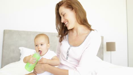 Smiling-young-mother-feeding-her-baby-girl-her-bottle