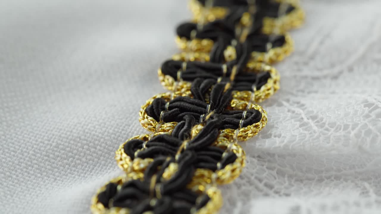 Elegante passamaneria decorativa nera e oro su tessuto bianco