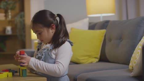 young girl at home playing with colourful wooden building blocks 2