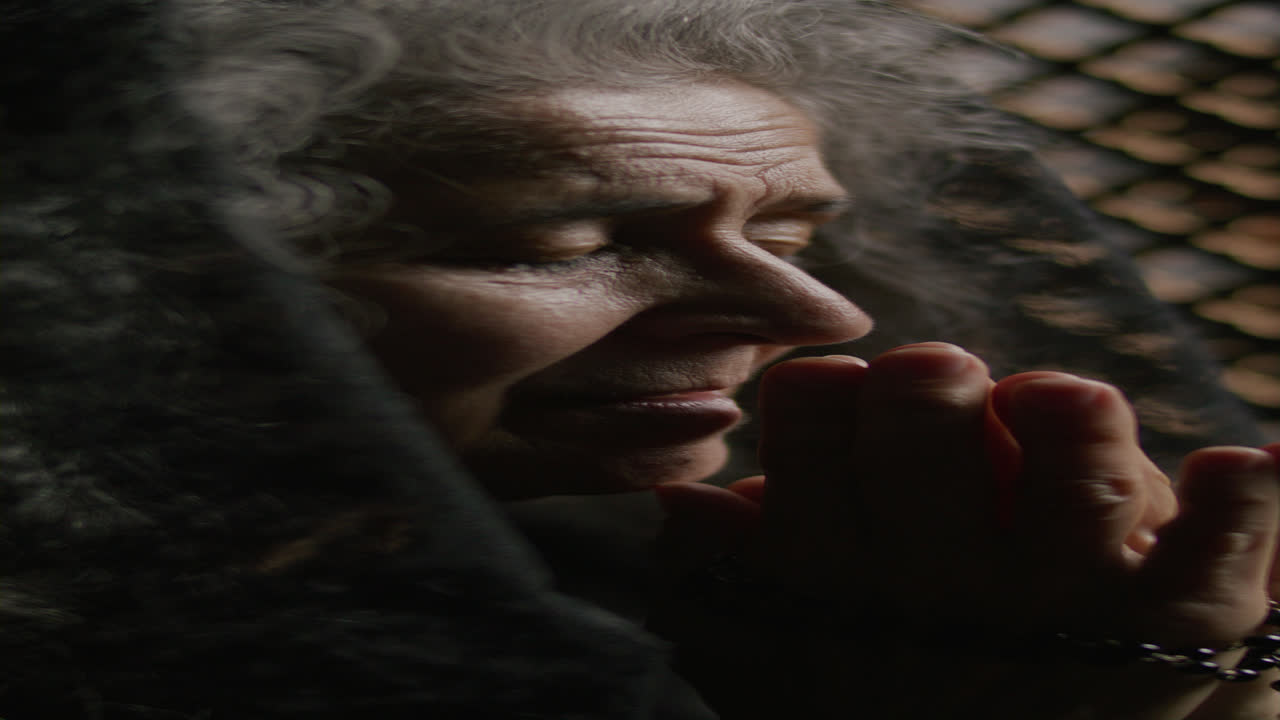 Senior Woman Whispering Prayer with Rosary in Hand during Confession