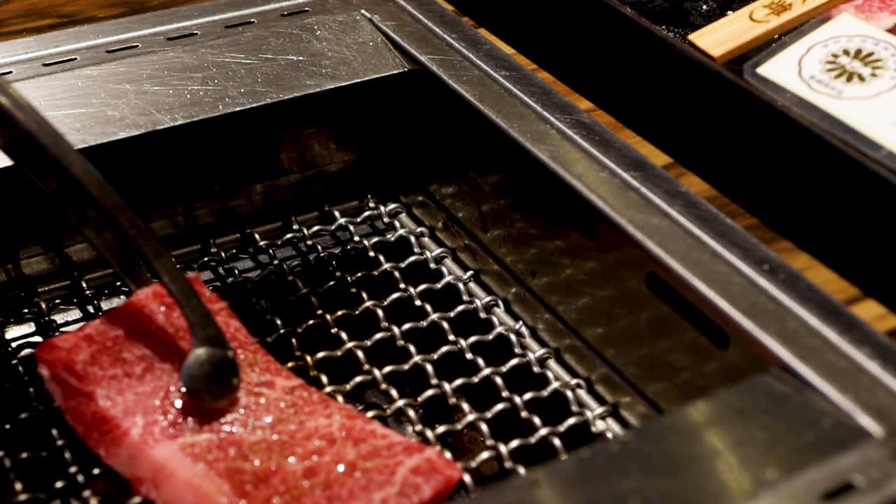 霜降りの多いPremium生牛肉のスライスを、熱い炭火焼きグリルに丁寧に並べています。