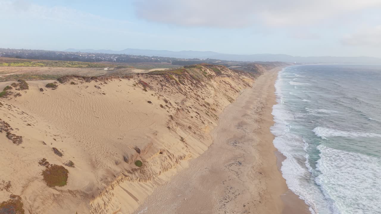 Aerial shot rising over sand dunes, revealing the coastline and ocean waves near Marina, California