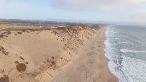 aerial shot rising over sand dunes, revealing the coastline and ocean waves near marina, california