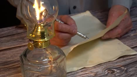 person writing with a vintage quill pen next to an oil lamp