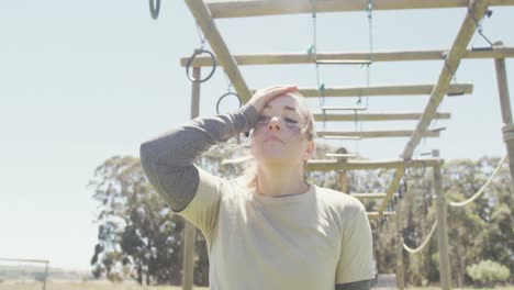 tired caucasian female soldier on climbing frame at army obstacle course in sun