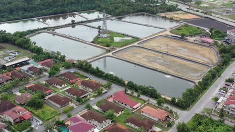 Barrio-Residencial-De-Sobrevuelo-De-Drones-En-Manjung,-Vista-De-Pájaro-Con-Vistas-A-Las-Instalaciones-Controladas-De-Acuicultura-Circundantes-Con-Torre-De-Transmisión-En-El-Medio,-Malasia,-Sudeste-De-Asia