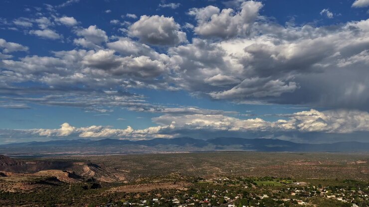 Timelapse 4K de dron capturando el borde de White Rock en el condado de Los Álamos, Nuevo México. Formaciones de nubes masivas e impresionantes flotan sobre la comunidad residencial local y el extenso desierto alto