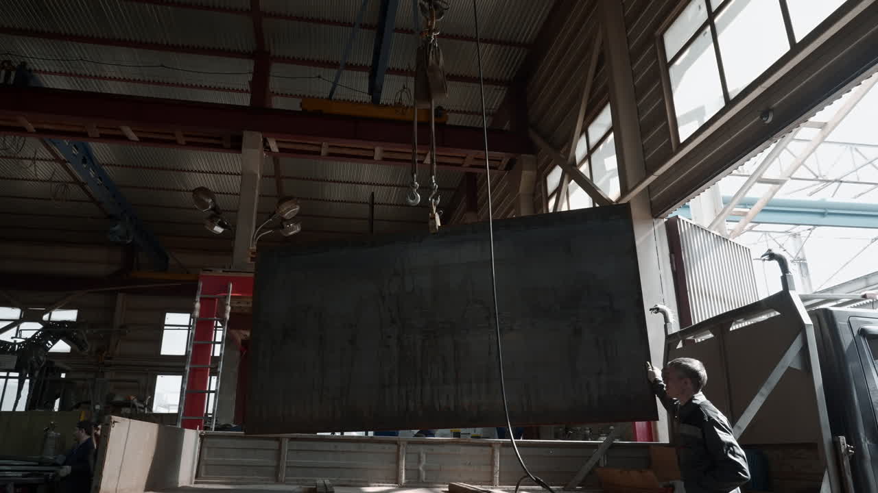 trabajador industrial cargando una gran placa de metal en un camión usando una grúa