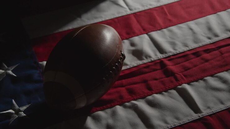 Toma de estudio con iluminación de clave baja de balón de fútbol americano sobre la bandera de barras y estrellas 9