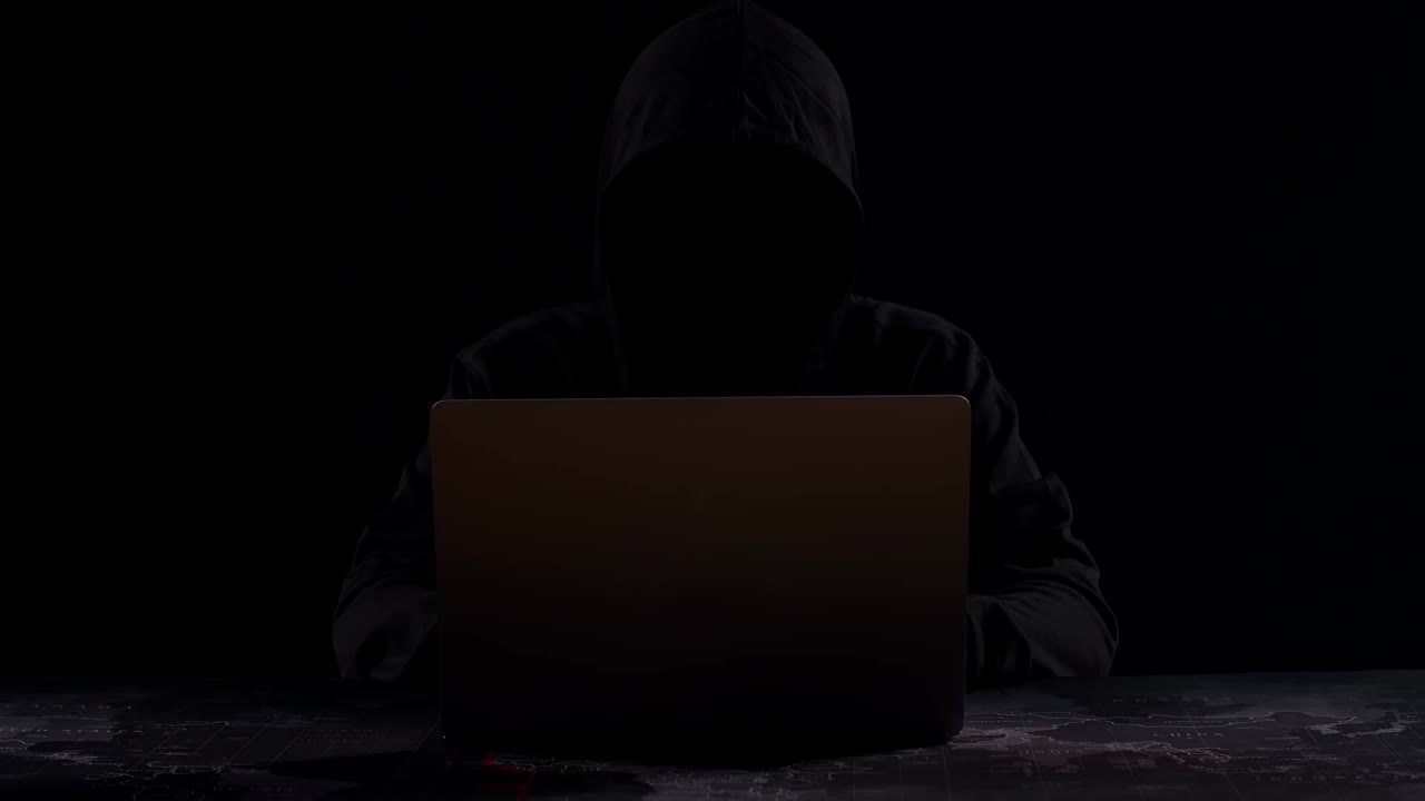 Person with a hoodie using a laptop in a dark room