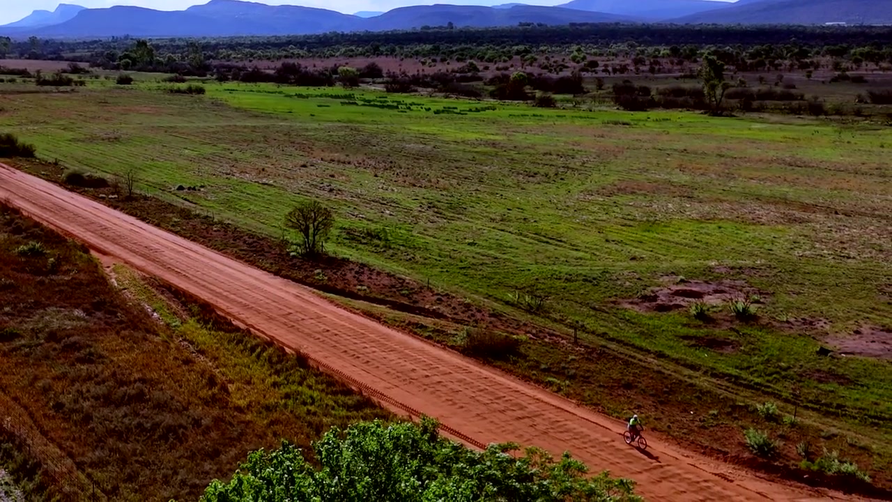Persona africana in bicicletta verso il lavoro su una strada sterrata in campagna. Drone.