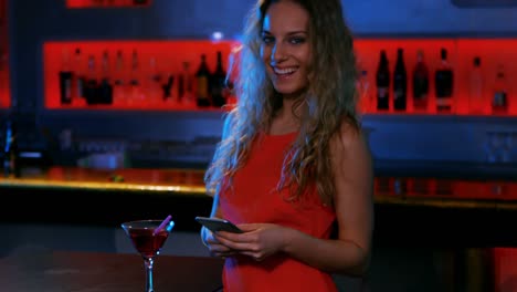 una mujer elegante enviando mensajes de texto en el bar.
