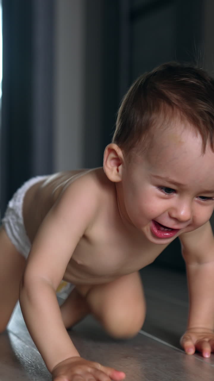 Happy smiling adorable baby in diaper crawls by the room. Black cat follows the child. Vertical video