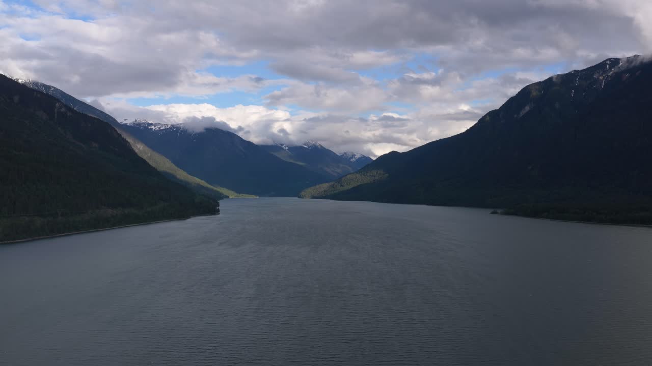 A serene lake nestled amidst tree-covered mountains in British Columbia, under a cloudy sky.