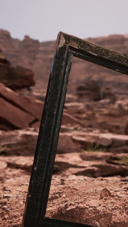 a wooden picture frame lies on the ground in the desert, with red rocks in the background.