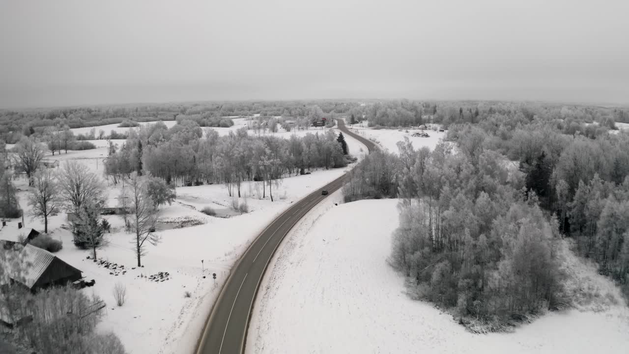 Car driving on a winding road in countryside landscape with snow covered ground and frost on the trees. Aerial European winter scenery with frozen forest.
