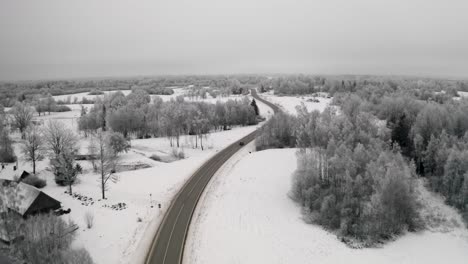 car driving on a winding road in countryside landscape with snow covered ground and frost on the trees. aerial european winter scenery with frozen forest.