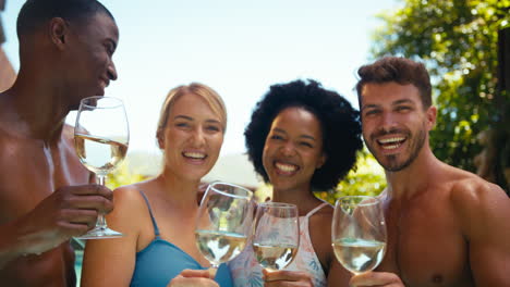 portrait of group of smiling multi-cultural friends on holiday in swimming pool drinking wine