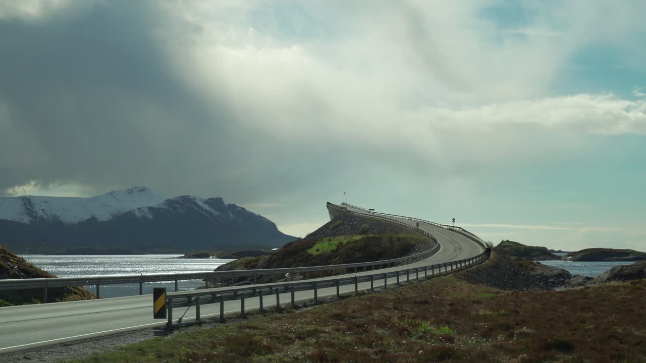 A view of the famous Atlantic Road in Norway. One of its'  arched bridges towering above the sea. The white mass of clouds hanging above the snow-covered mountains