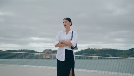 Smart-lady-talking-wireless-earbuds-standing-in-front-gray-cloudy-sky-vertical