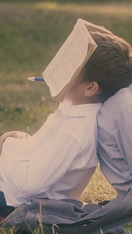 tired schoolmates in shirts and jeans sleep with books in hands sitting on school yard lawn at break closeup slow motion