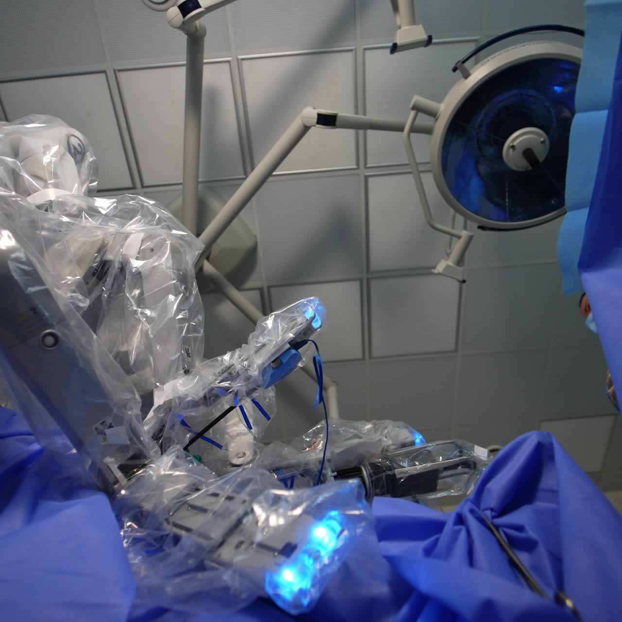 Surgeon system robotic arms covered I plastic operate the patient. Medical professionals watching the process carefully. Low angle view