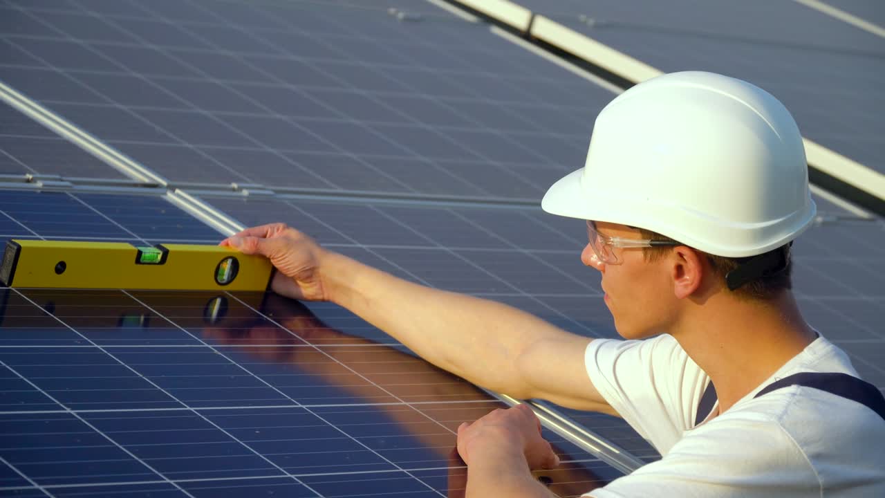 Engineer male inspector in a white helmet check the vertical level of the solar panel by spirit level. Solar panel technician working with solar panels. The green energy concept