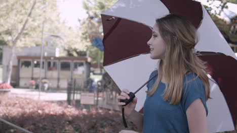 Millennial-woman-holding-an-umbrella-and-standing-in-the-park-by-the-carousel