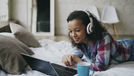 young woman relaxing on bed, working on laptop