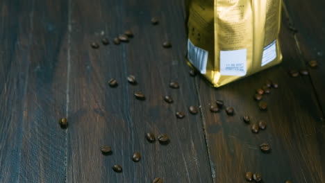 hand of a black man grabbing a cup of steaming coffee next to a packet of coffee beans on a wooden table