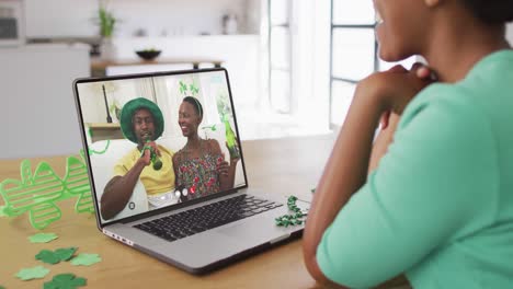 una pareja afroamericana sonriente con cerveza vistiendo artículos en forma de trébol en una videollamada en una computadora portátil