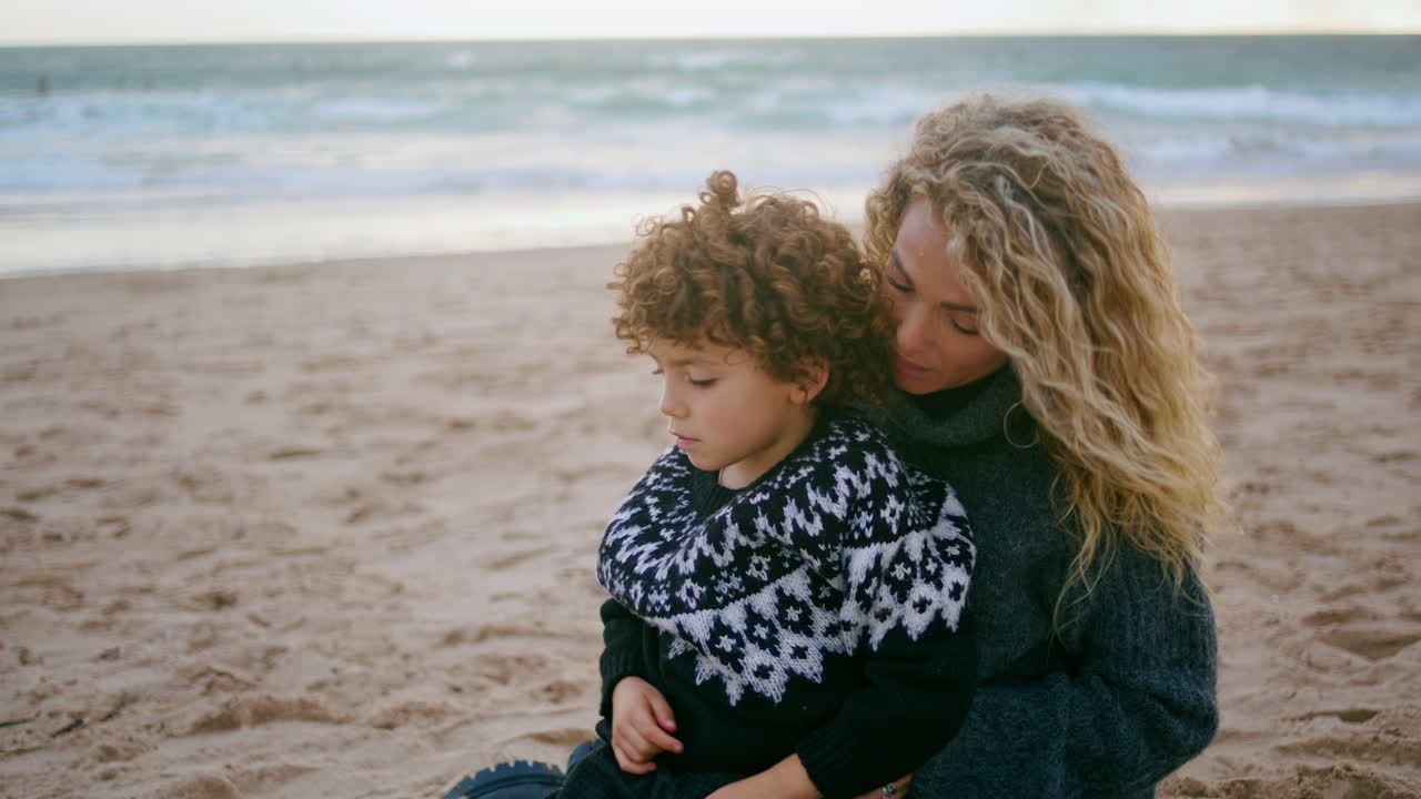 Mutter deckt Kind mit Decke bei kaltem Strandpicknick Nahaufnahme. Bedingungslose elterliche Liebe.