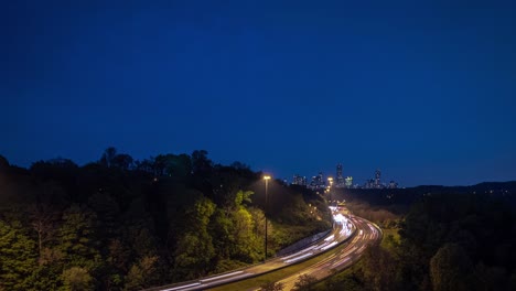 a vertically panning timelapse long exposure light trails and traffic on a curved highway road leading towards the downtown toronto skyline at night with trees lining the sides of the road.