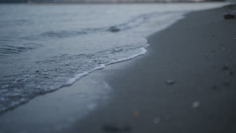 Low-angle-gentle-waves-lapping-on-sandy-beach-at-dusk,-nature-background