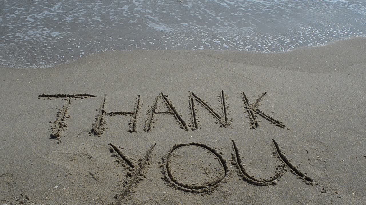 Obrigado escrito à mão na areia de uma praia. Filmagem na praia