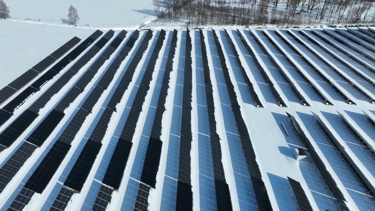 Dron letící bokem nad panely solární elektrárny v řadě na zasněžených polích, Estonsko.