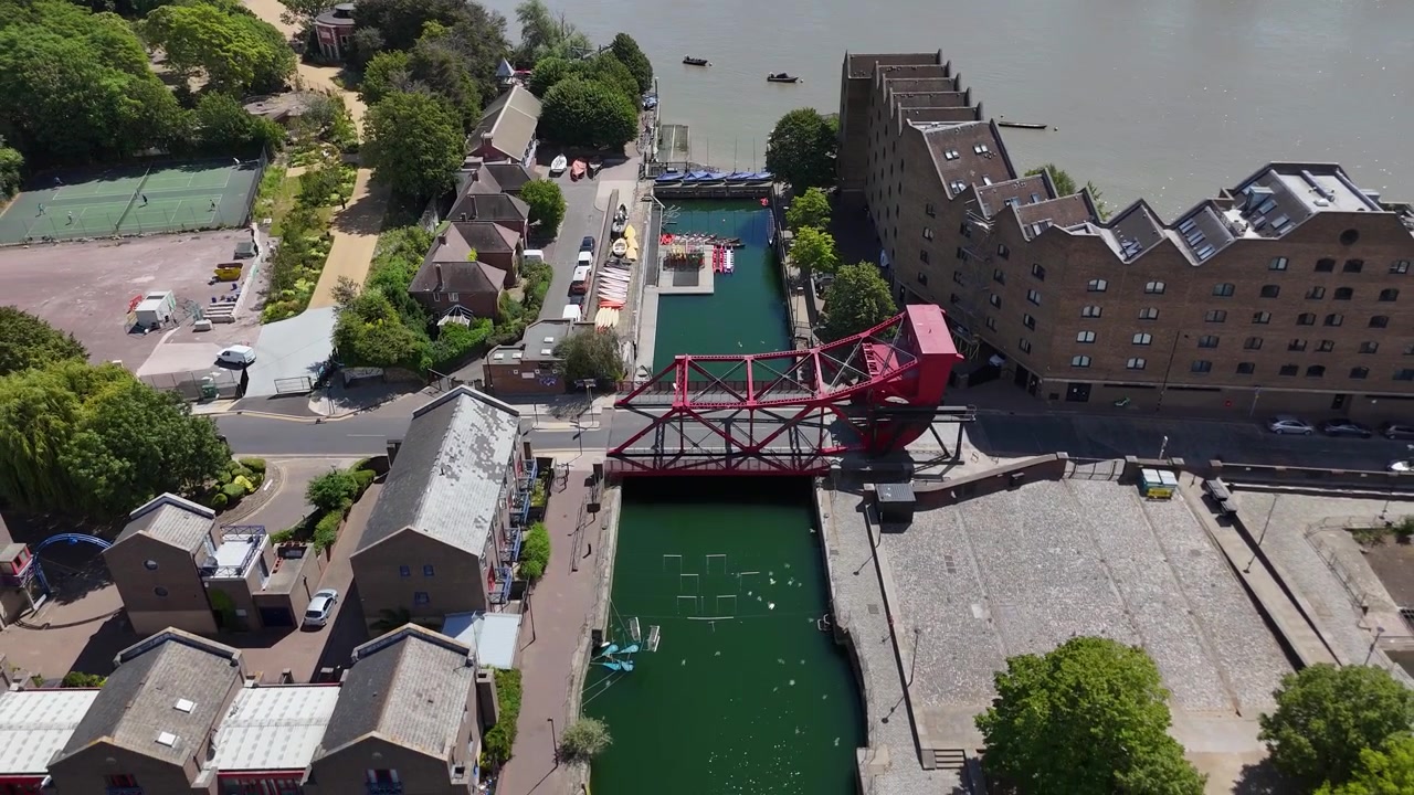 Ponte basculante in acciaio rosso attraversa uno stretto canale del molo tra edifici di magazzini convertiti e una strada lungo l'acqua