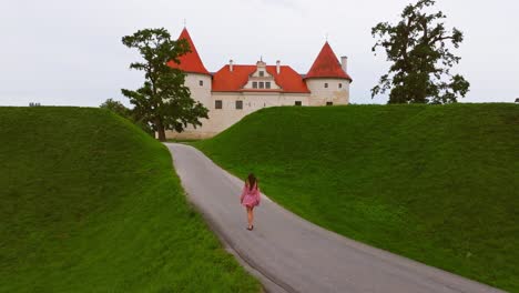 wide aerial shot of woman walking alone to medieval bauska castle in latvia