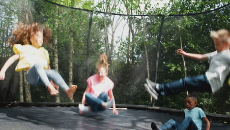 group of children having fun with friends bouncing on trampoline in garden