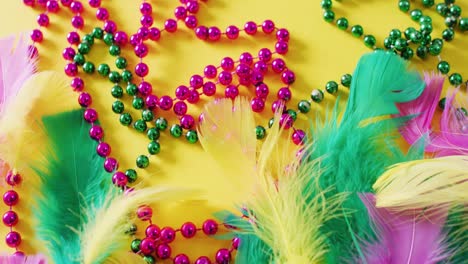 video of pink and green mardi gras carnival beads and feathers on yellow background