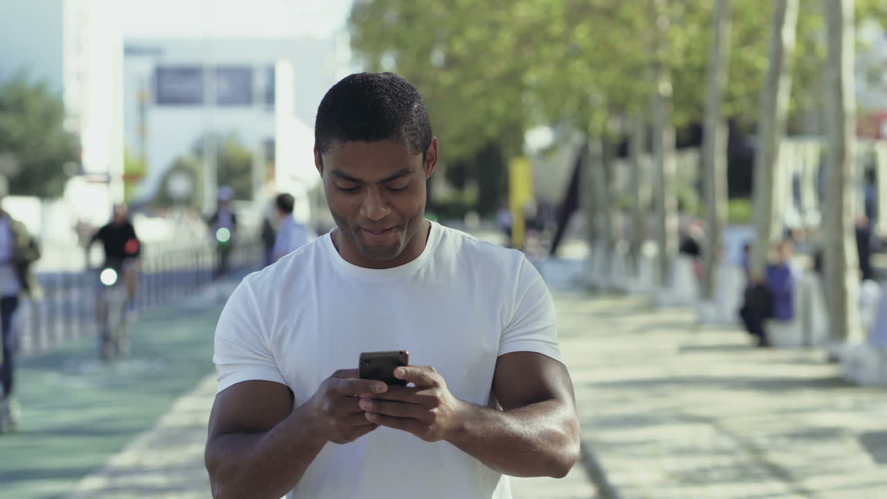 Smiling muscular sportsman with smartphone during stroll.
