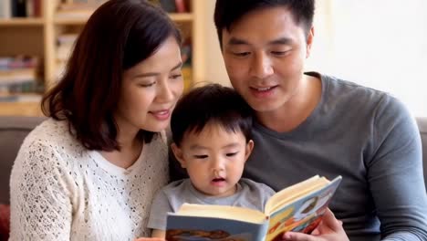 asian young parents with their young son reading a storybook in the living room.