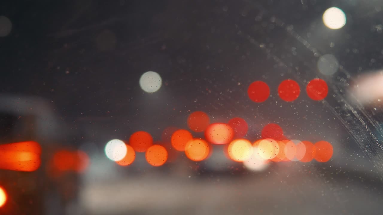 밤에는 도시 조명과 함께 흐릿한 도시 풍경, 흐릿한 배경, 도로에서 기계를 타고, 도시에서 눈이 내리고, 차 앞 유리 기기는 창문에서 눈을 청소합니다.