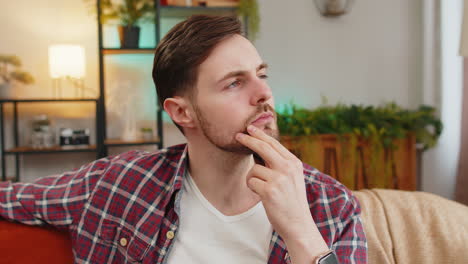 Thoughtful-Caucasian-man-sitting-at-home-looks-pensive-thinks-over-life-concerns-or-unrequited-love