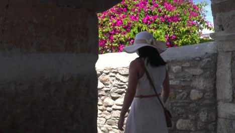 slide reveal of girl in beautiful white summer dress walking through arch in alley with flowers in background