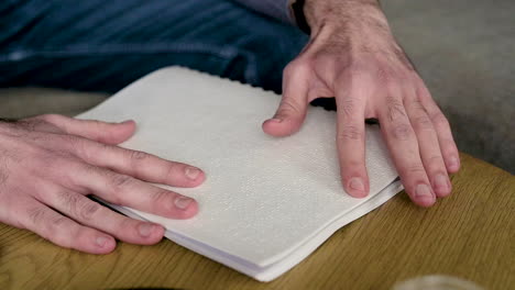 The-Camera-Focuses-On-Man-Hand-Reading-A-Braille-Book-Sitting-On-The-Sofa-At-Home-1